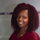 black woman with red hair and top smiles at the camera