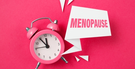 Pink alarm clock with papers and text menopause on pink background