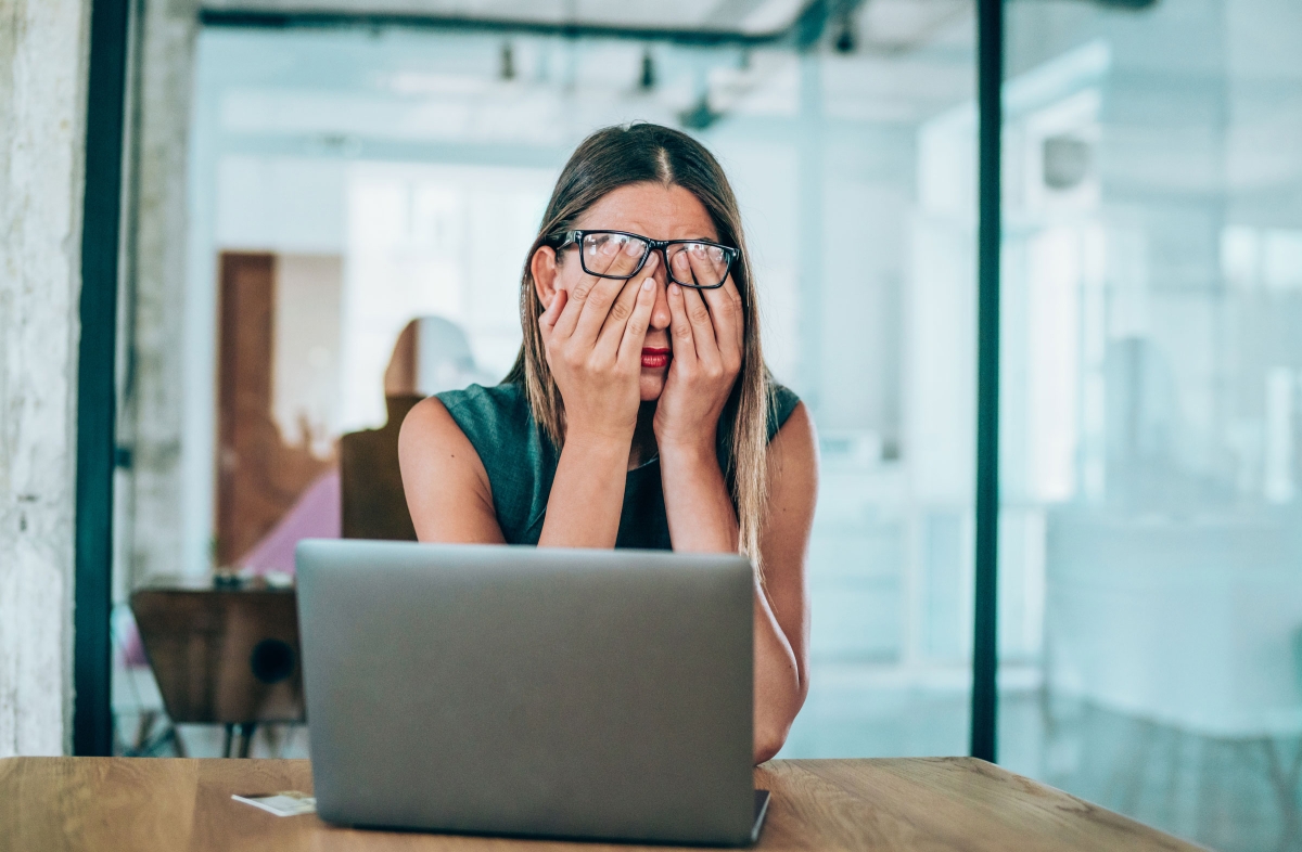 Woman at work in an office looking stressed with head in hands