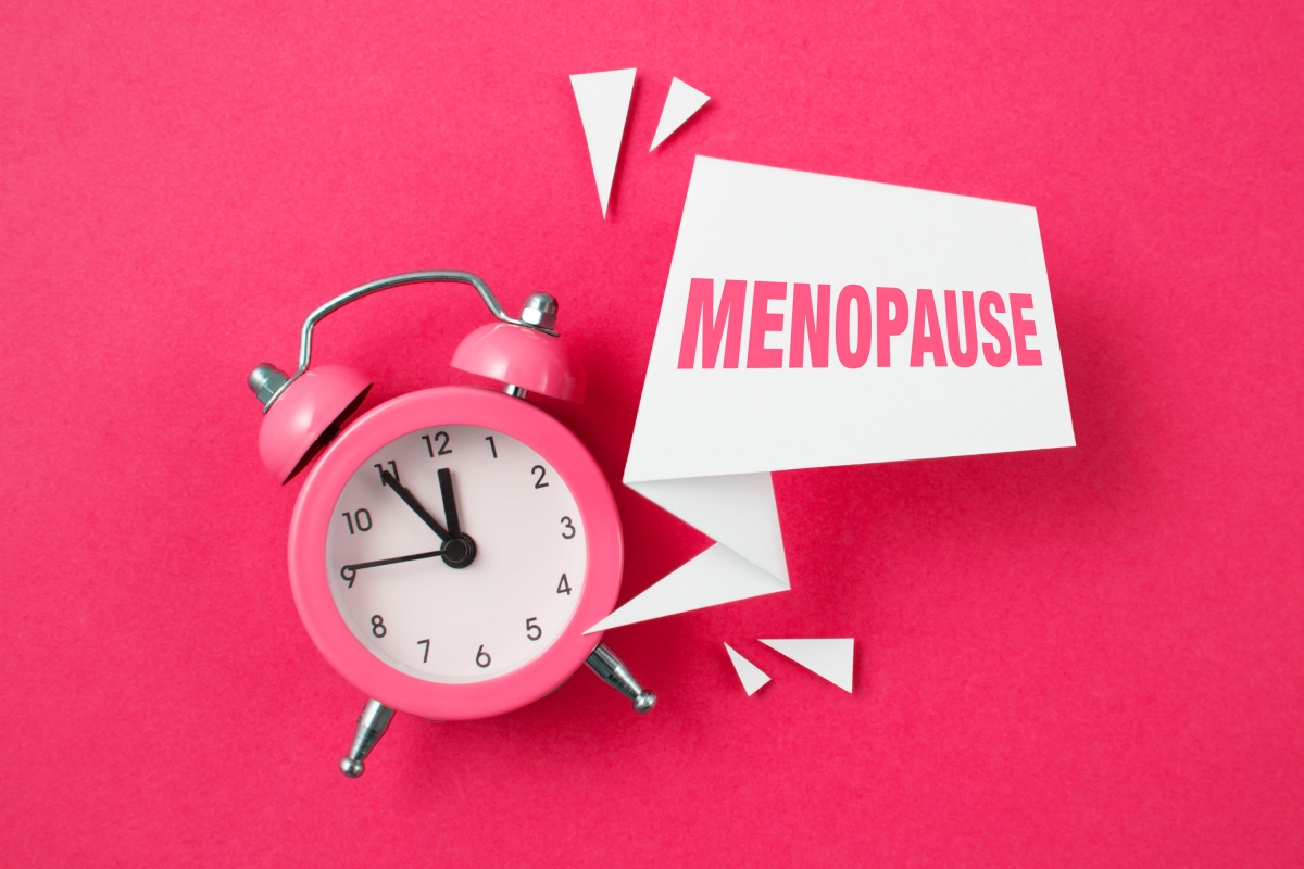 Pink alarm clock with papers and text menopause on pink background