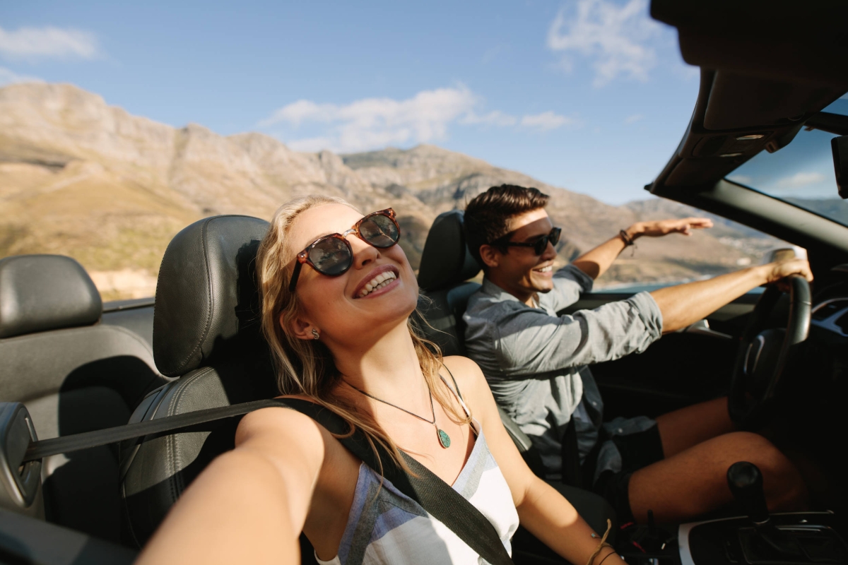 Happy couple driving a convertible car through a mountain road on a sunny day