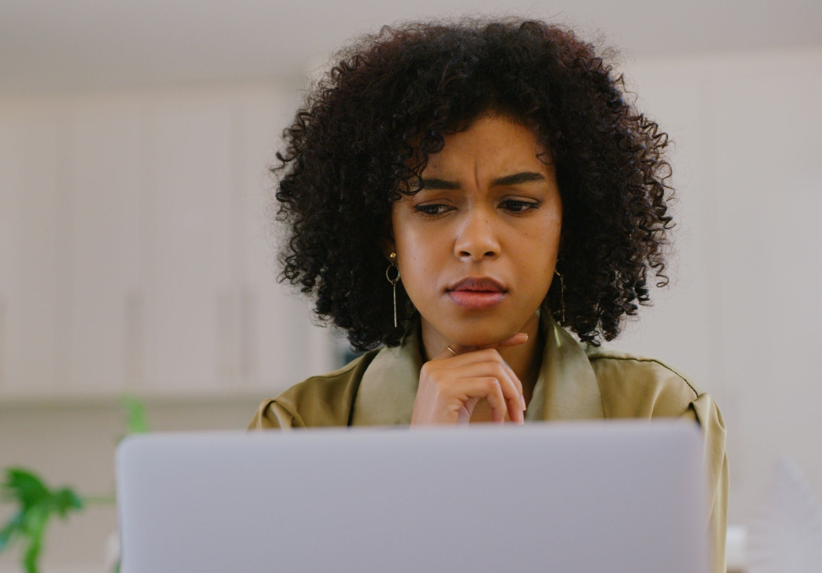 Shot of a young woman looking confused while using a laptop at home